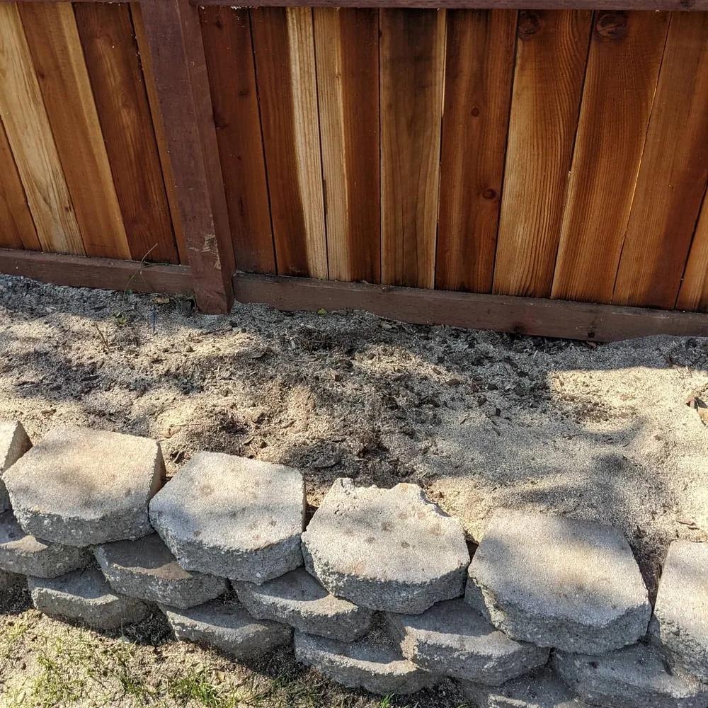 Ground area after stump grinding beside a wooden fence